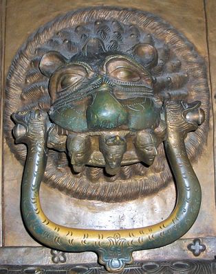 DRZWI PŁOCKIE - detal
Kołatka (antaba) lewego skrzydła drzwi, należy do wyjątkowych - w paszczy lwa umieszczono aż pięć głów ludzkich, z których środkowa nosi mitrę biskupią. W średniowieczu, lwia paszczcza symbolizowała piekło.
Słowa kluczowe: katedra drzwi