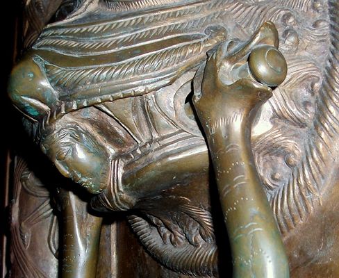 DRZWI PŁOCKIE - detal
Fragment kołatki prawego skrzydła, piekło pochłania lub wypluwa postać, której głowa widoczna jest w paszczy lwa (Lucyfera). Ruchomą część kołatki trzymają smoki połączone ogonami.
Słowa kluczowe: katedra drzwi